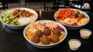Three freshly prepared halal platters with grilled chicken, falafel, hummus, pita bread, rice, fresh salad, and creamy sauce, showcasing high-quality ingredients at a halal restaurant.