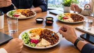 Colleagues enjoying halal platters with seasoned rice, grilled meat, hummus, pita bread, and fresh salad.