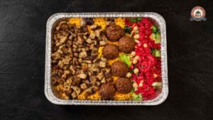 Halal platter with seasoned chicken, rice, falafel, and fresh salad served in a takeaway tray.